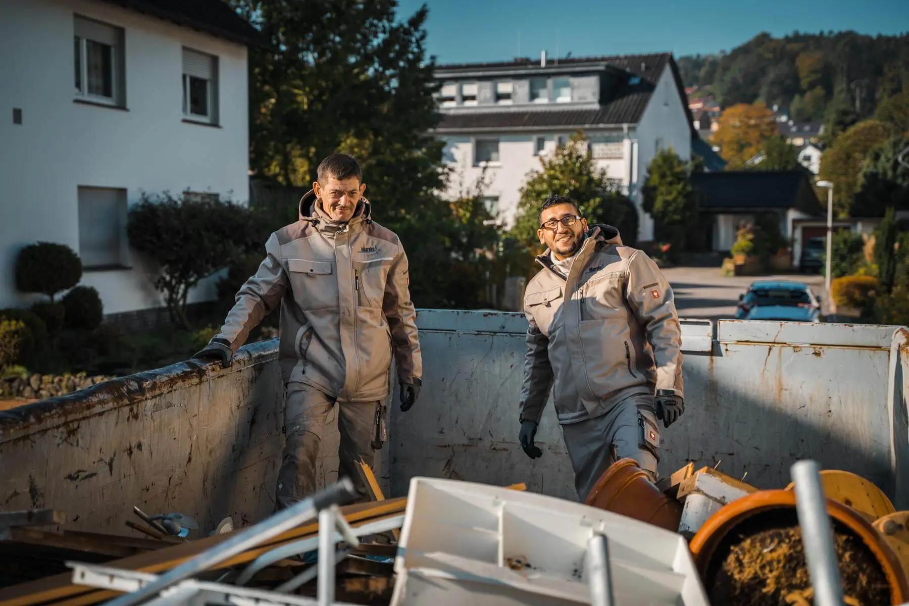 Zwei Mitarbeiter von Mazreku haben Spaß bei der Arbeit in einem Container während einer Entrümpelung und Entrümpelungen.